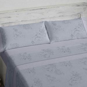 Juego de sábanas estampado con un diseño de finas flores perfiladas en gris sobre fondo azul. Bajera lisa azul. Confección encimera y almohada con aplique de la bajera más ribete a juego (una sola almohada para cama de 90, 105,120,135 y dos para cama de 150, 160,180, 200). Confección bajera ajustable.